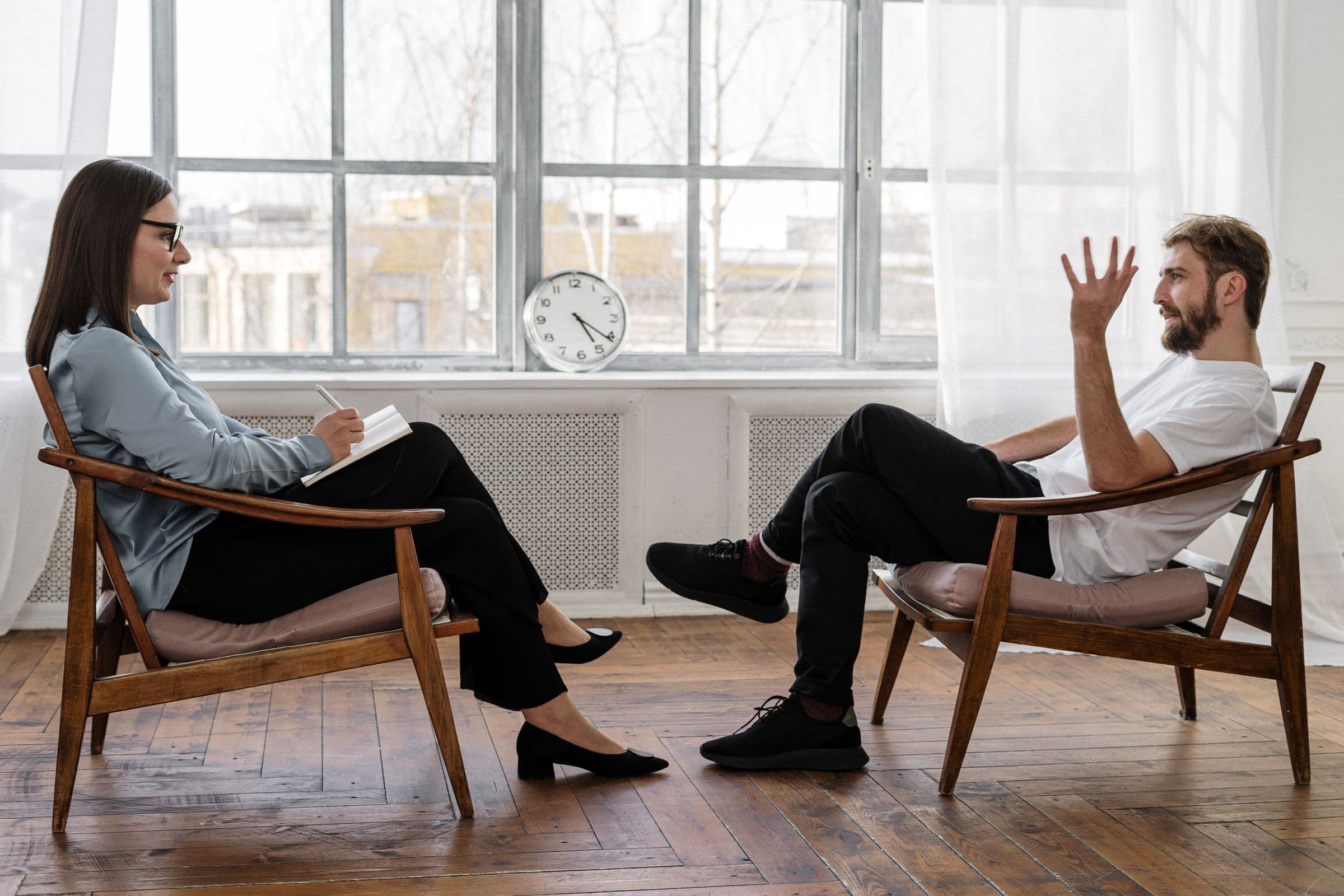 Two people talking in armchairs by a window